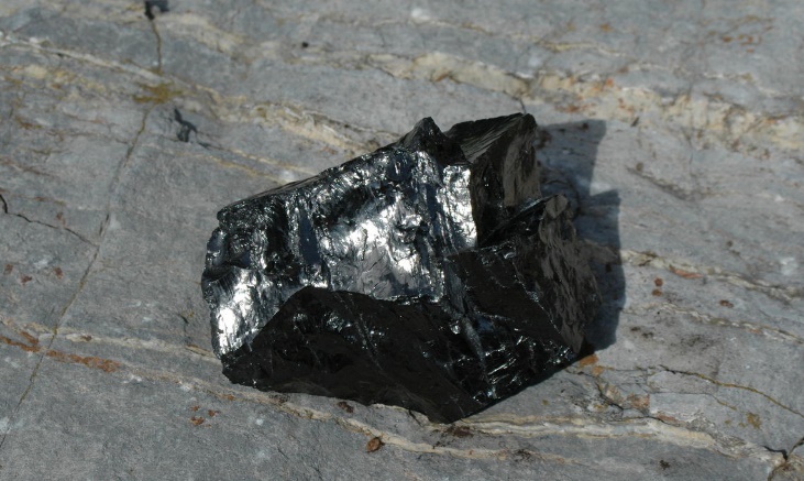 Image shows a sample of anthracite coal on a rock backdrop