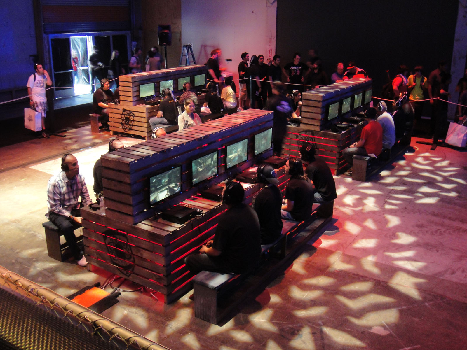 Color photograph of twenty-four players, mostly white and evidently male, of Call of Duty at a "Zombie Challenge" convention in Los Angeles in two thousand eleven. They are seated at computer stations and presumably fighting zombies in the wildly popular video game, while other conventioneers stand in line behind them awaiting admission.