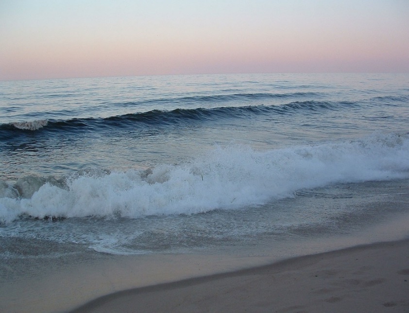 The sky fades from blue to pink as small waves break along the beach.