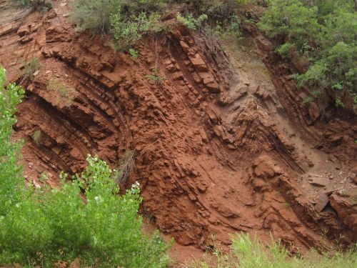 Sedimentary layers of red rock appear to be folded into an S-curve.