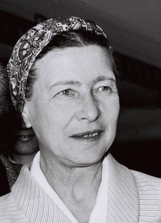 Black and white photograph of the great twentieth-century existentialist and feminist French philosopher Simone de Beauvoir, seen here smiling radiantly, well coiffed, bejeweled, and wearing a sweater-like blouse.