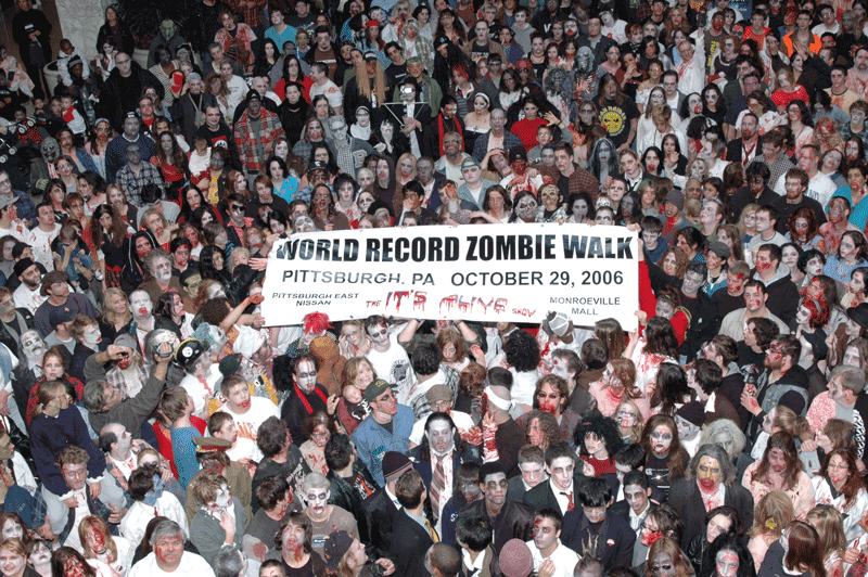Color photo from above by Miss DeeCS of about nine hundred zombie walkers set the world record in two thousand and six by gathering, adorned in fake blood, outside the Monroeville Mall, near Pittsburgh, where George Romero’s Dawn of the Dead had been filmed in nineteen seventy-seven, released the following year.