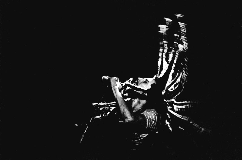 Black and white photograph of Jamaican reggae musician Bob Marley on stage, singing with such inspiration that his dread locks cast high above his head, reminiscent of a lion's mane, one of the most important symbols in Rastafari.